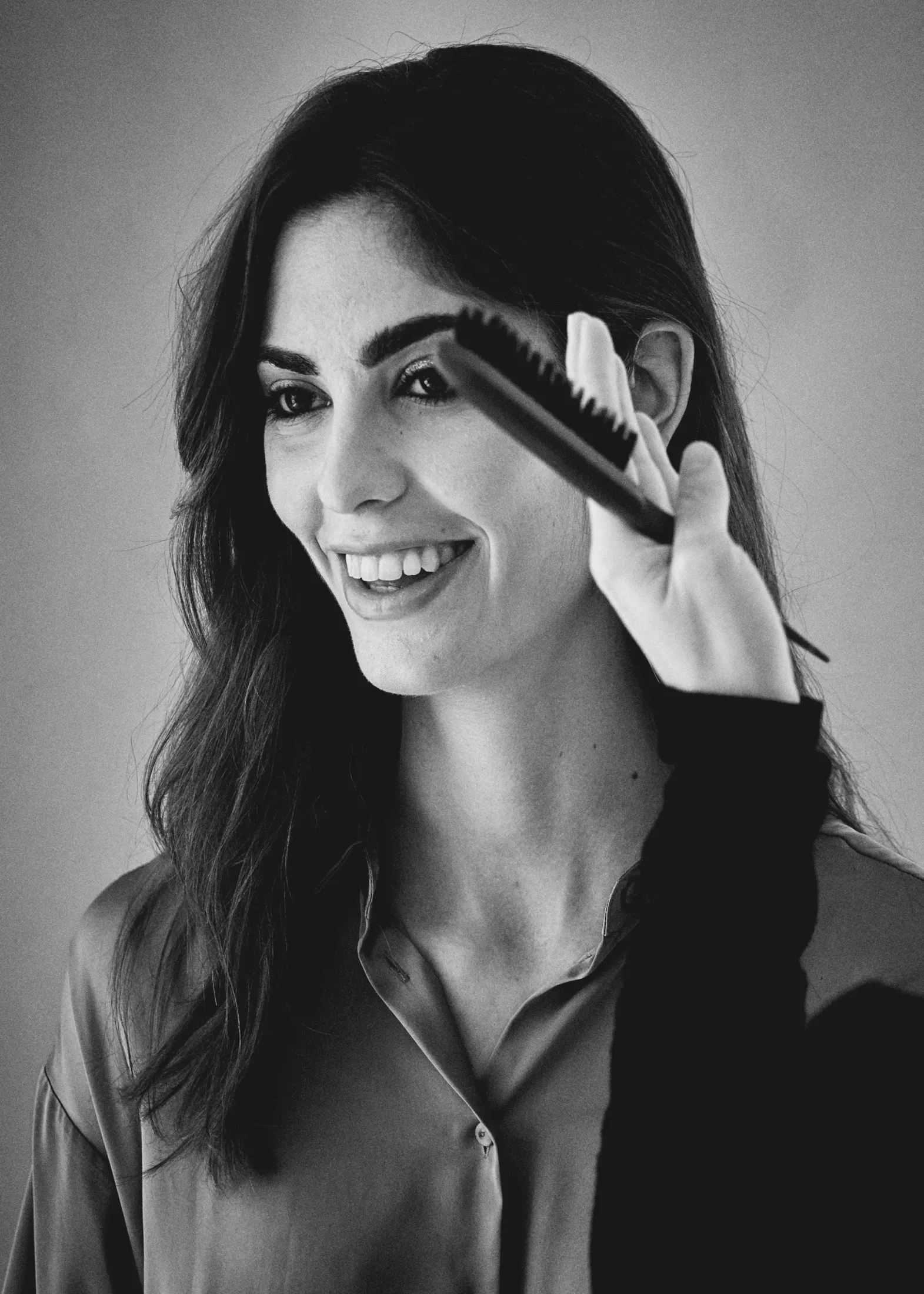 Modelo sonriendo mientras le retocan el maquillaje con un pincel, en blanco y negro